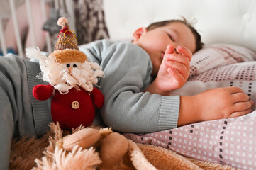 Sweet caucasian toodler boy sleeping in his bed next to a toy gnome. Christmas morning concept.