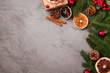 Christmas composition. Gift box, balls, cinnamon, anise, dried fruits, pine cones and fir needles decorations on grey background. Top view copy space