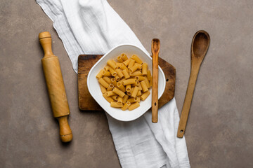 Top view of dry fusilli pasta on white plate with wooden spoons and rolling pin.