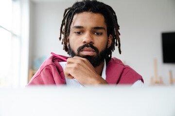 Focused african american guy working with laptop while sitting in office