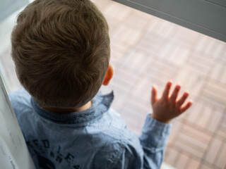 Little boy looking through a glass window during the coronavirus pandemic