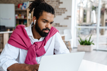 Serious african american guy in earphones working with laptop