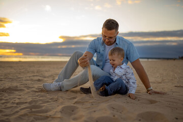 Dad and son are playing with sand on the beach at sunset. Image with selective focus. Father's day concept