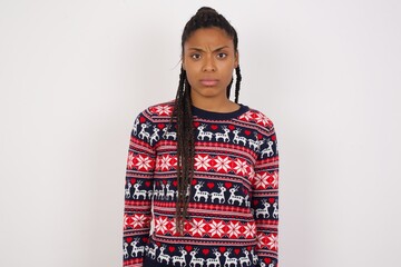 Young beautiful African American woman wearing Christmas sweater against white wall frowning his eyebrows being displeased with something.