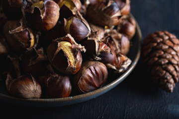 Roasted chestnuts in ceramic dish on dark background. Winter background.