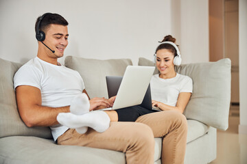 Brunette man and lovely lady sitting on couch with laptops