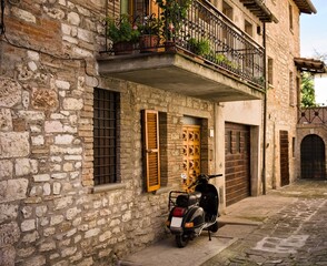 Fototapeta na wymiar An isolated scooter parked in the courtyard of an old stone house of a medieval italian village (Gubbio, Umbria, Italy, Europe)