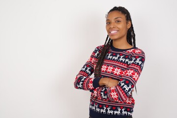 Image of cheerful Young beautiful African American woman wearing Christmas sweater against white wall with arms crossed. Looking and smiling at the camera. Confidence concept.