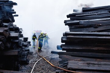 Firefighters with breathing apparatus intervene in the smoke during a fire on old railway sleepers
