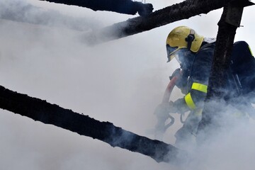 A firefighter in a mask with a breathing apparatus intervenes in smoke during a fire on the roof of...