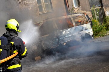 Firefighters extinguish a burning van with water from a hose
