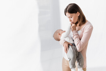 mother holding in arms infant boy and kissing tiny hand