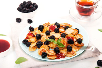 Mini-pancake dessert with blackberries, decorated with mint leaves, jam and tea in a glass bowl, two forks on a white plate. Healthy breakfast.