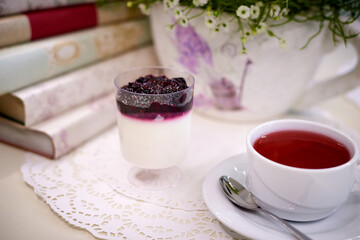 Blueberry dessert with red tea on the table with flowers and books.
