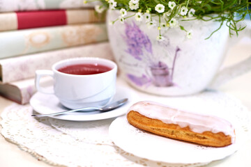 Cake with tea on the table with flowers and books.