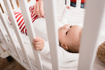 hand of father near infant son in baby crib on blurred foreground