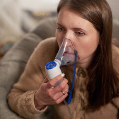 woman makes inhalation nebulizer at home. holding a mask inhaling fumes spray the medication into...