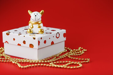 New year's 2021 toy bull with a gift on a red background. Gift box and gold beads.