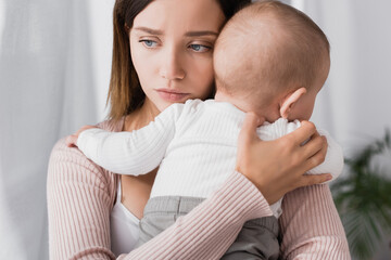 worried mother holding in arms baby boy and looking away