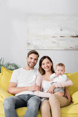 happy parents smiling near baby boy while sitting on sofa