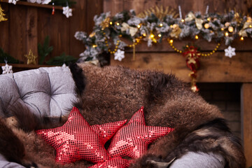 The comfort of Christmas in front of the fireplace arm chair with leather in dark colors. fur skin lying on a rattan chair. red pillows with shiny elements are sewn in the shape of a star