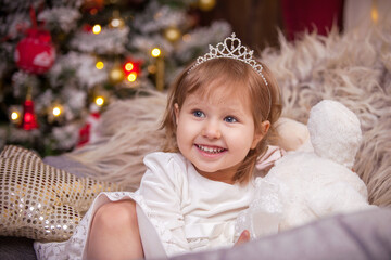 the girl smiles, a Christmas tree in the lights and a window with a garland surrounds the atmosphere of the holiday