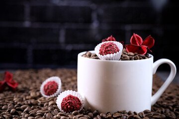 White cup full of coffee beans , red flowers and red chocolate candy against the background of a dark brick wall. Morning espresso. Coffee mug.