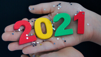 Child holds in his hand multi colored numbers 2021 on a black background. Festive New Year and Merry Christmas concept