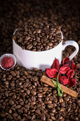White cup full of coffee beans on a coffee beans background with red flowers , red chocolate and cinnamon. Morning espresso. Coffee mug.