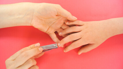 Hands cuts child's nails. Close up and pink background