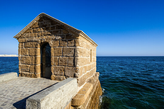 Tide gauge in front of sea with clear blue sky and buildings in the background.