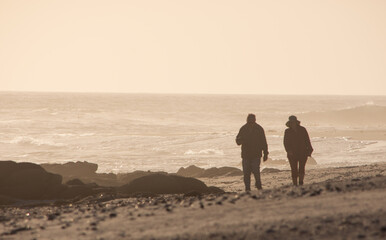 Two people walking together though the mist of a rocky beach near sunset