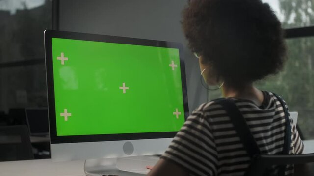 Over The Shoulder Shot Of a Business Woman Working In Office Interior On Pc On Desk, Looking At Display Green Screen. Office Person Using Computer With Computer Green Screen, Sitting at Table.