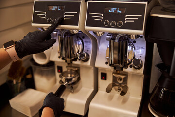 Experienced barista using modern coffee-grinder at work