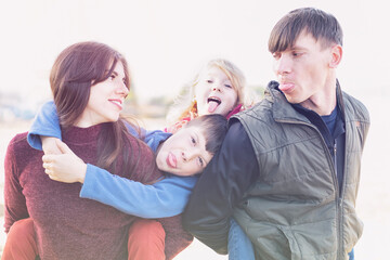 Parents and two kids having fun together - Family of fooling around and showing tongue - Dad mom and two kids hugging together happy family concept