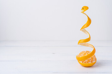 Mandarine mit geschälter Schale als fliegende Spirale geformt, auf weißem Holztisch
