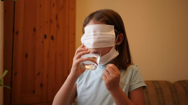 Kid girl funny play drink water with antivirus disposable mask on her mouth and eyes