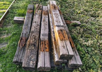 Fototapeta premium Old, discarded long wooden sleepers for railway repairs are scattered casually on green grass for garbage, recycling. Preparatory work.