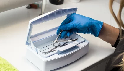 Foto op Canvas Woman in blue gloves sterilizes manicure tools in the nail tool sterilizer machine. Safe concept. Safe manicure and pedicure. Image for beauty salon and sites about manicure. Beauty sphere. © anasttrofimova20