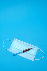 Syringe and disposable face mask to prevent COVID-19 virus on blue background