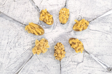 Various pasta on spoons on a white stone background. different sort pasta on spoons laid out in a circle.
