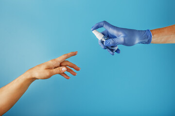 A hand in a glove with a disinfectant spray treats an unprotected hand without a glove on a blue background.