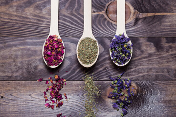 Dried myosotis Mallow flower herbal tea, Green tea and Rose flowers on spoons on wooden table