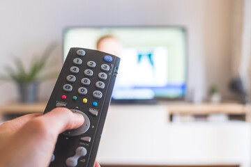 Male hand is holding TV remote control, streaming on a smart TV.