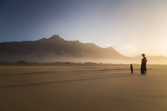 Silhouette of young mother with her little child walking on sunshine in Cofete, Fuerteventura, Canary Islands, Spain.