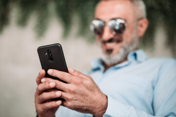 Portrait of middle age man with beard and with sunglasses looking at the phone.