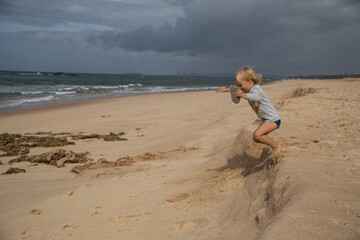Boy jumping from small sand dune on beach in Portugal.