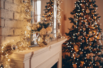 White classic fireplace with decorations against of Christmas decorated tree with sparkling garlands