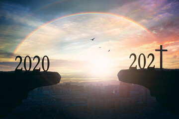 2021 concept: Silhouette of year 2021 and cross  on mountain  with city sunset  background