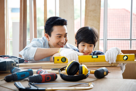 Father teach son using level tool in woodwork.